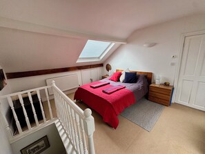 A bedroom with a sloped ceiling, a skylight, a bed with a red blanket, a nightstand, a wooden dresser, and a white door. - Gorgeous 3-bedroom townhome on Endcliffe Park (Sheffield)