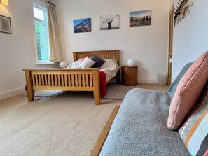A bedroom with a bed, a wooden bench, a grey sofa, a small round table, and wall-mounted artwork. - Gorgeous 3-bedroom townhome on Endcliffe Park (Sheffield)