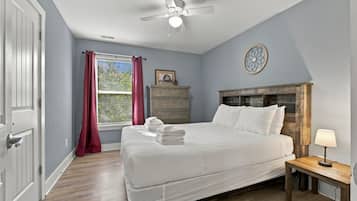 Un dormitorio con cama, mesita de noche, cómoda, ventilador de techo y ventana con cortinas.