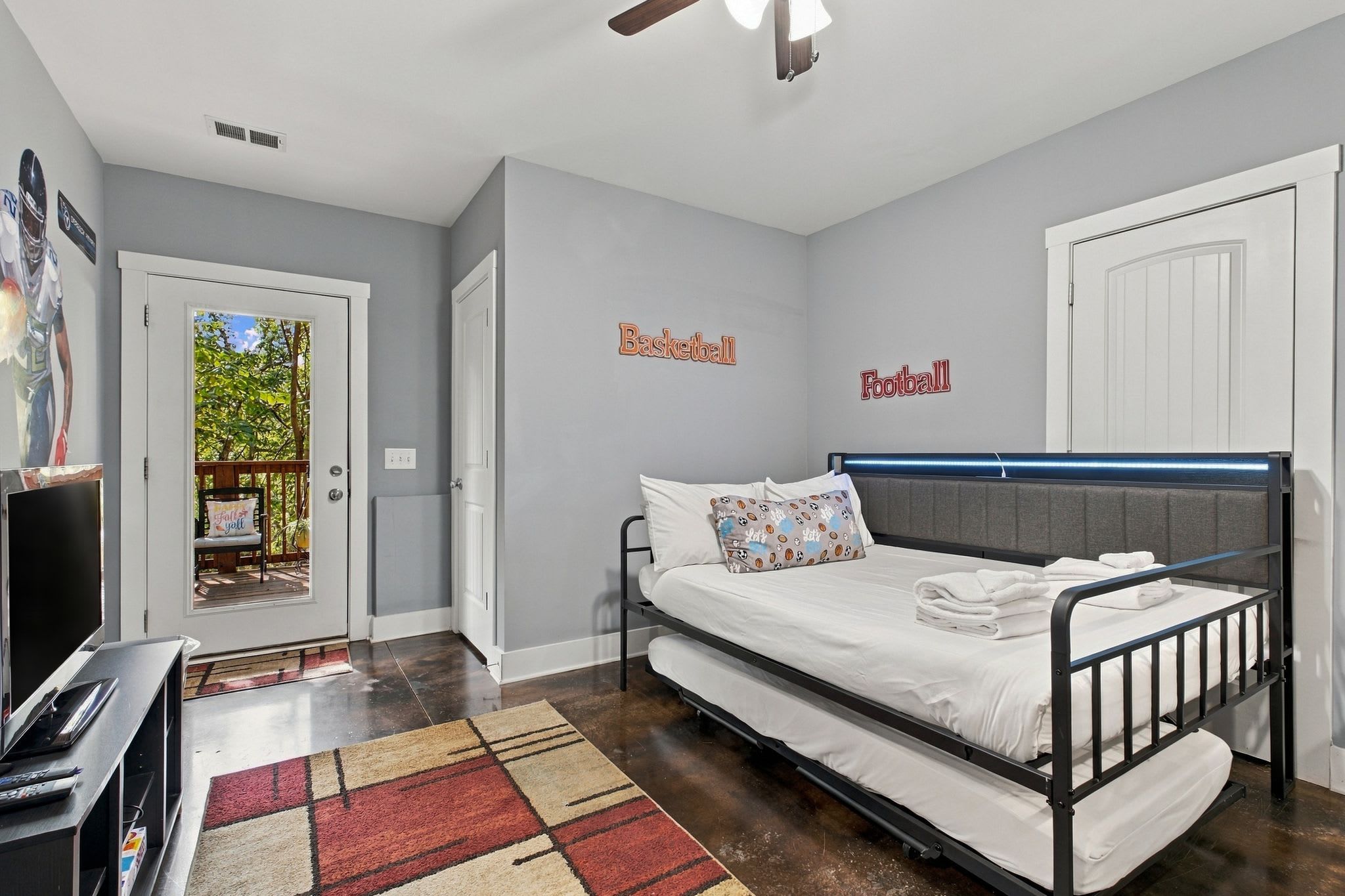 A bedroom with a bed, a desk, and a television. There are wall decorations for basketball and football.