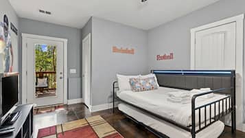 A bedroom with a bed, a desk, and a television. There are wall decorations for basketball and football.
