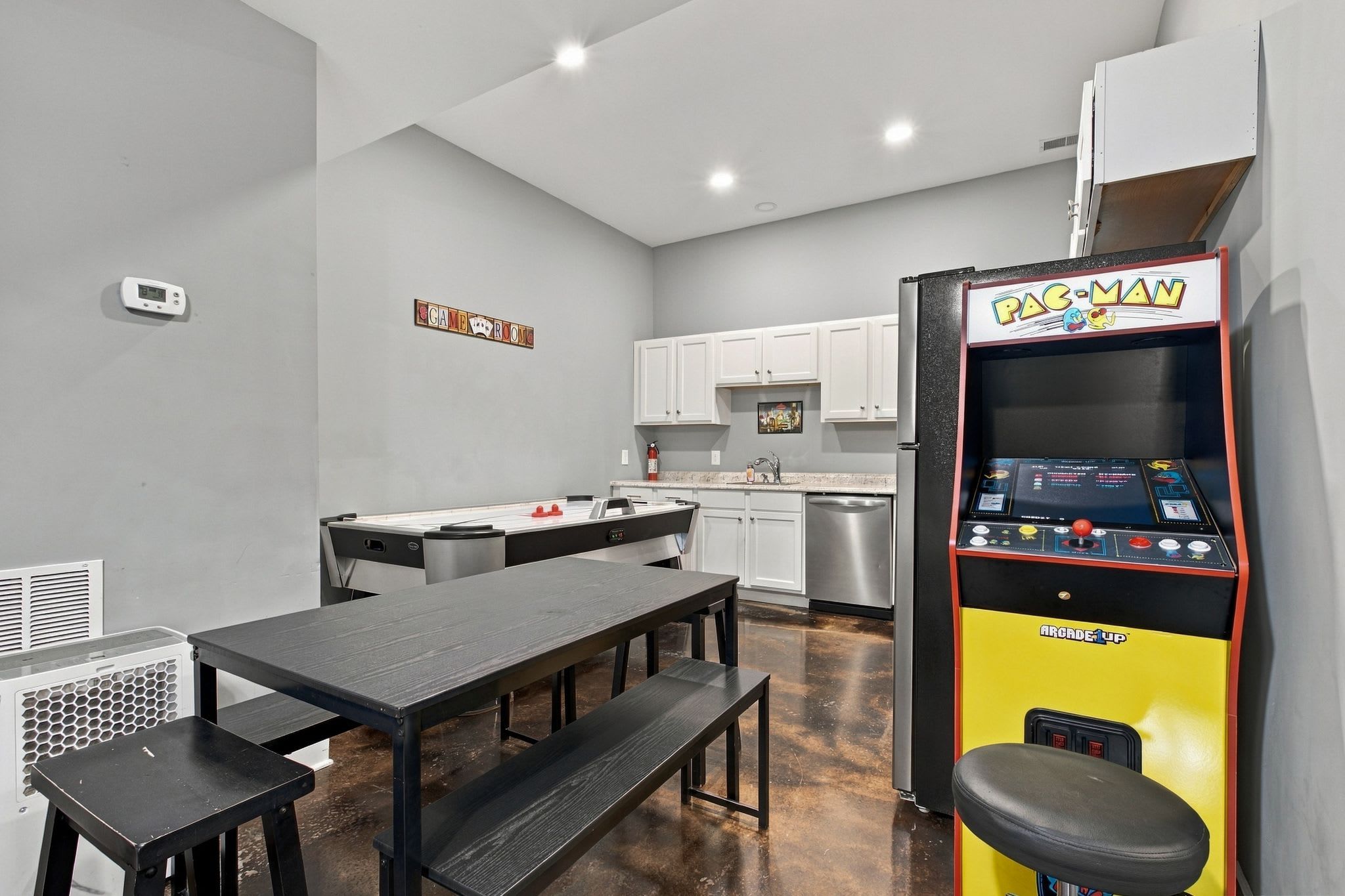 A compact kitchen with a dining area, a kitchenette, and a Pac-Man arcade machine.