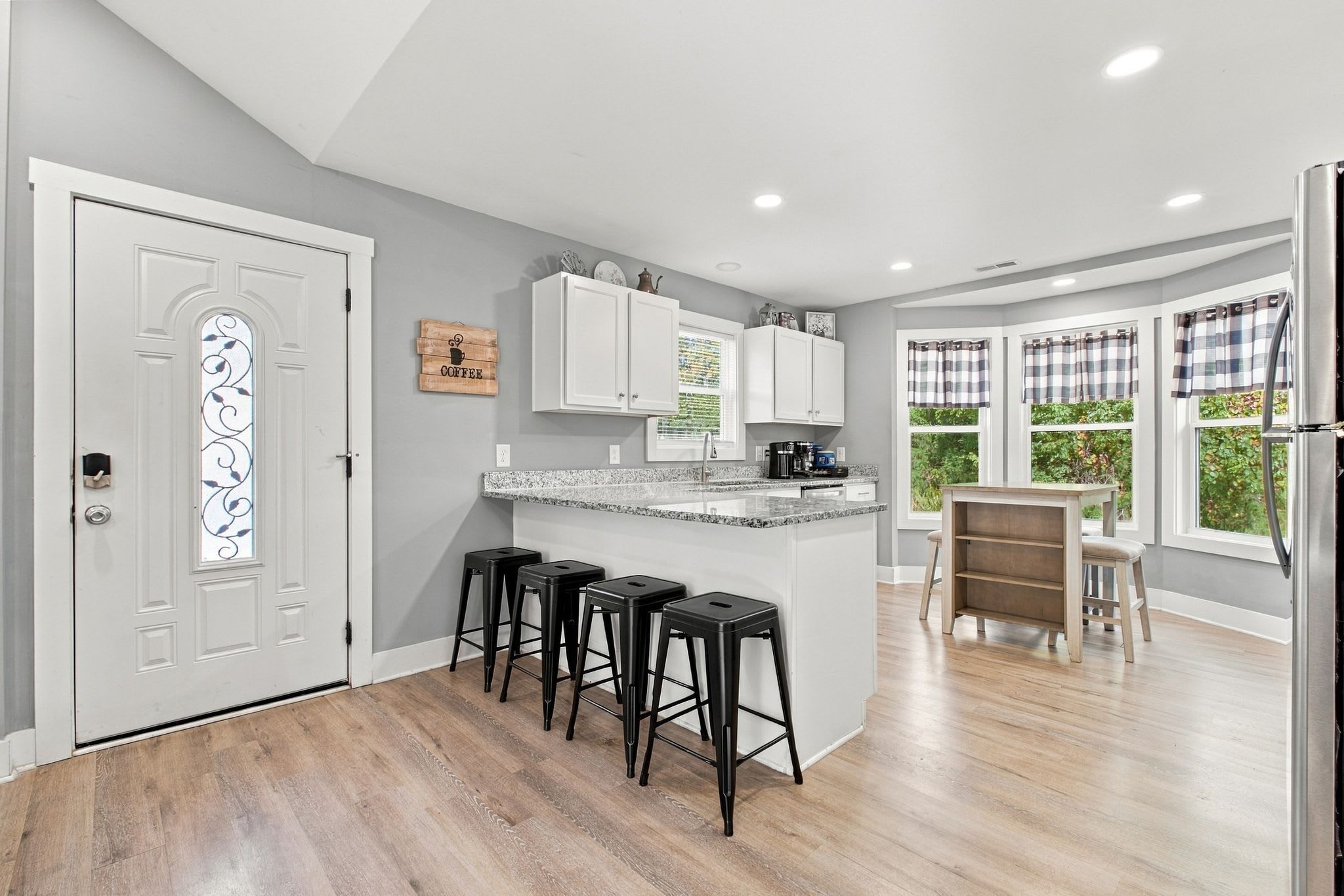 A modern kitchen with a central island, bar stools, and a dining area with a table and chairs.