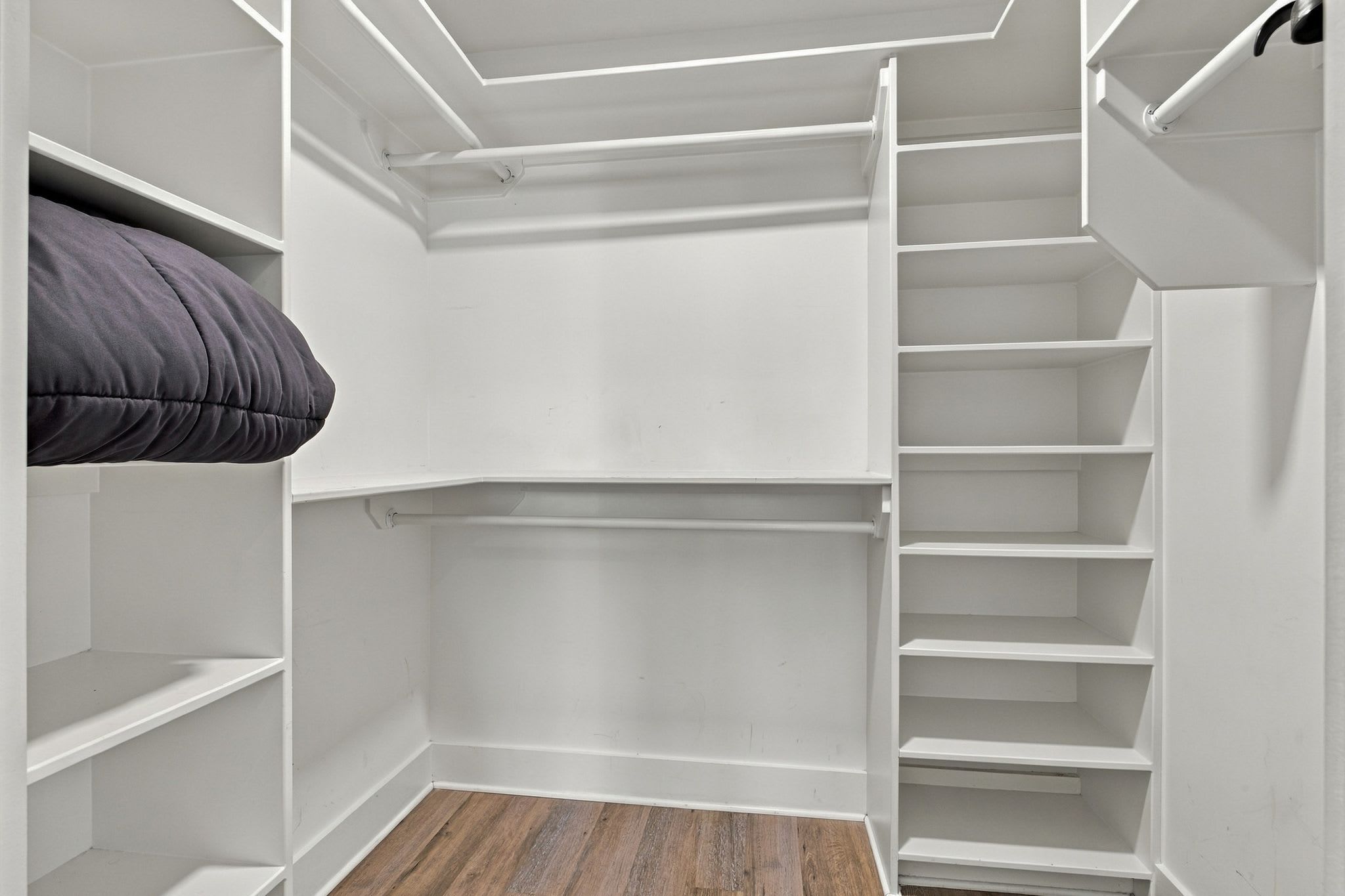 A walk-in closet with open shelves and a wooden floor.