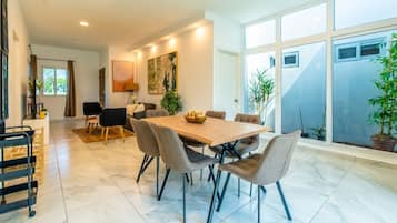 Un comedor con una mesa y sillas de madera, un cuadro en la pared y un ventanal con plantas.