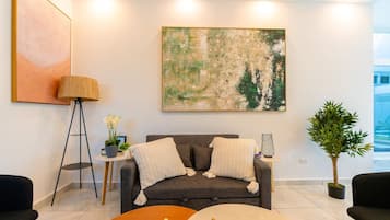Uma sala de estar moderna com um sofá cinza, uma mesa de centro, um abajur e uma grande pintura abstrata na parede.