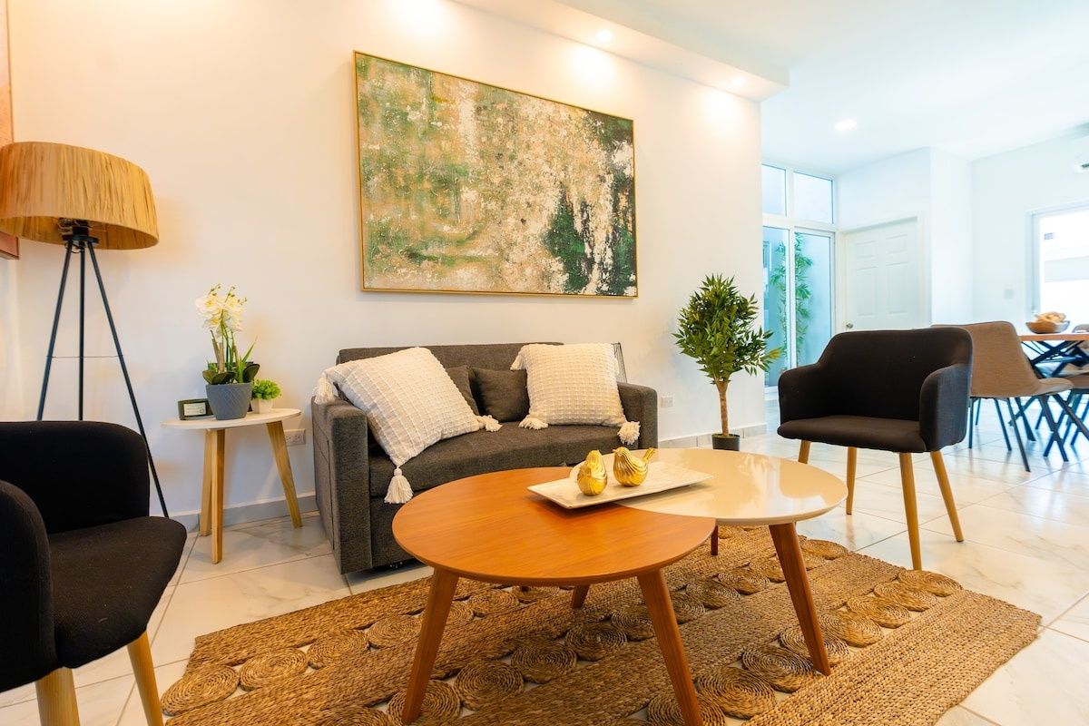 Un salon moderne avec un canapé, une table basse et des fauteuils, un tableau au mur et une petite table d’appoint sur laquelle est posée une plante.