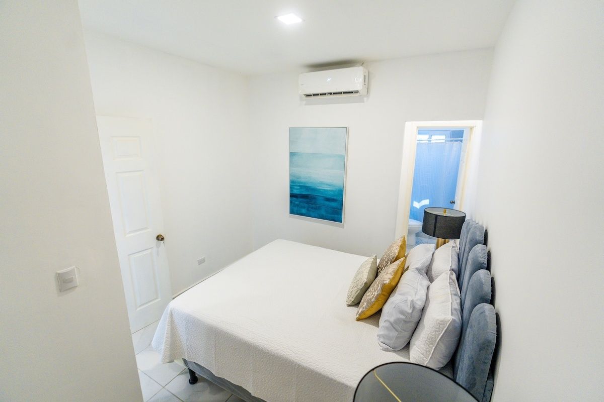 Un dormitorio con cama, aire acondicionado de pared, una puerta y una ventana con cortinas.