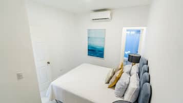 Un dormitorio con cama, aire acondicionado de pared, una puerta y una ventana con cortinas.