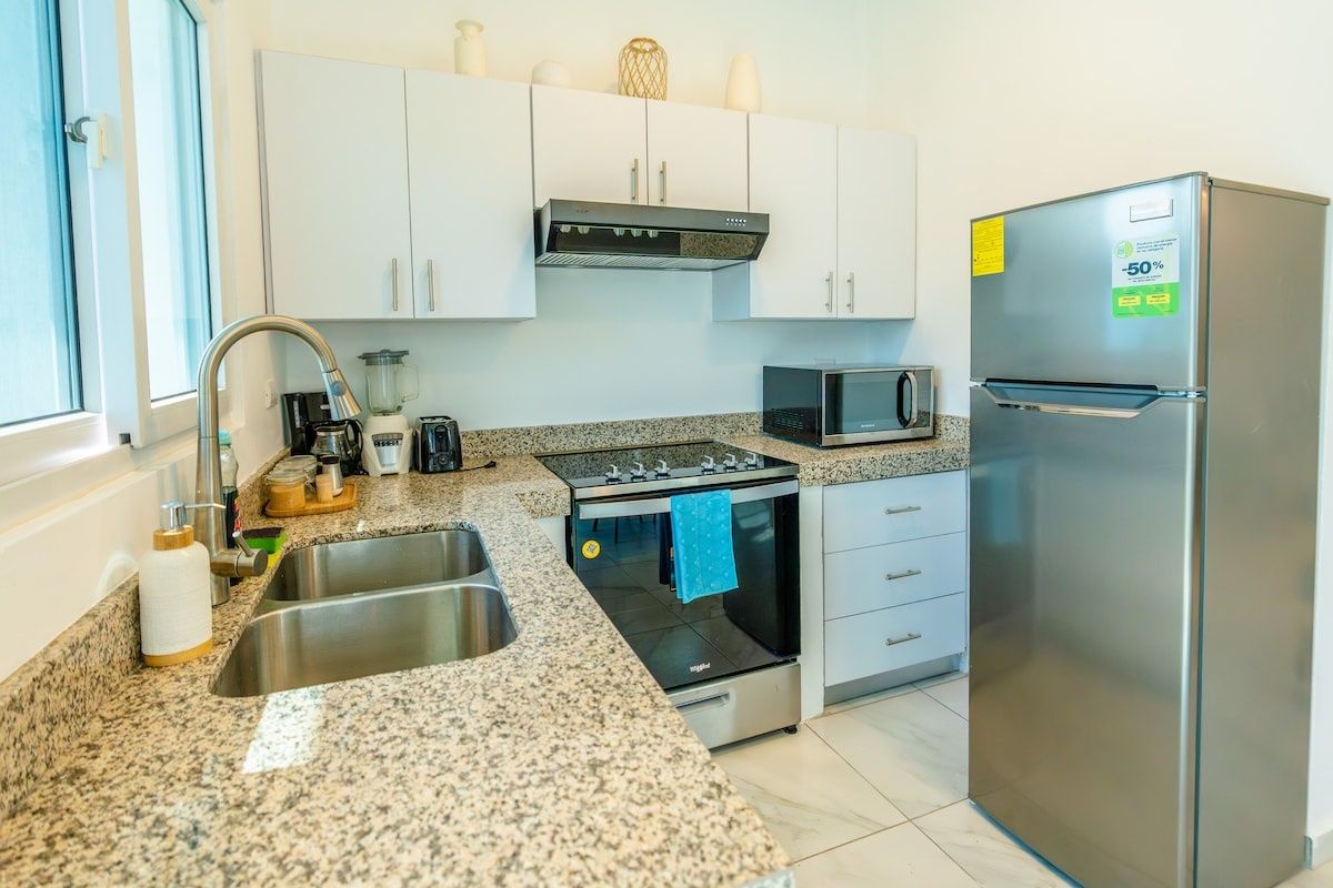 Una cocina moderna con electrodomésticos de acero inoxidable, encimera de granito y armarios blancos.