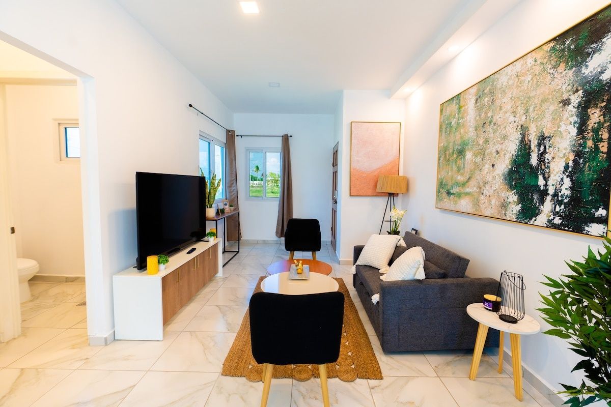 A modern living room with a flat-screen TV, a grey sofa, a coffee table, and a painting on the wall.