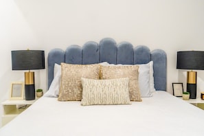 Een bed met een geborduurde hoofdbord, twee nachtkastjes met lampen, en decoratieve kussens.