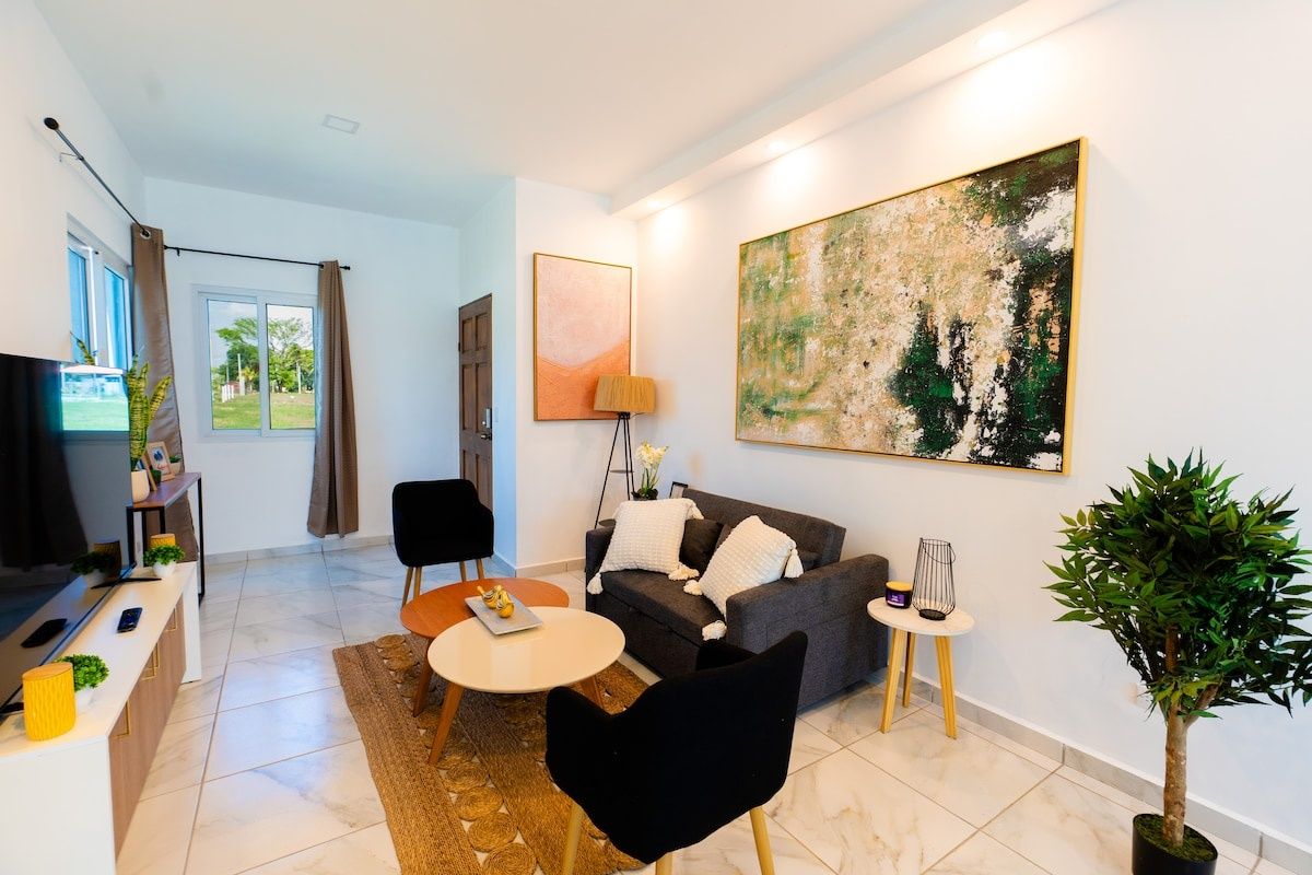 Una sala de estar moderna con sofá, sillas, una mesita de centro, televisor y obras de arte en la pared.