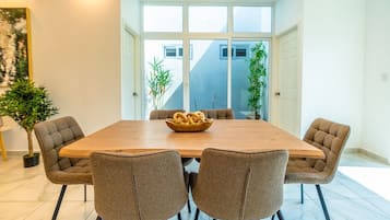 A dining area with a wooden table and four upholstered chairs, a bowl of breadsticks, and potted plants.
