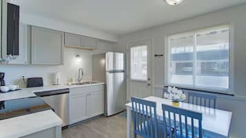 Een moderne keuken met witte kasten, een roestvrijstalen koelkast, een vaatwasser, en een eethoek met blauwe stoelen en een witte tafel.