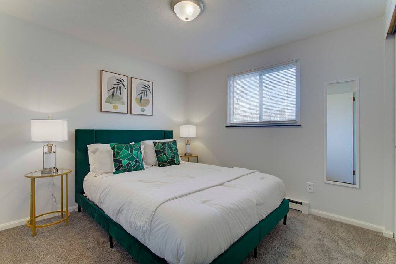 Une chambre à coucher comprenant un lit, deux tables de chevet, une fenêtre et deux cadres photo accrochés au mur.