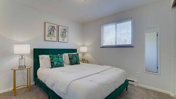 Une chambre à coucher comprenant un lit, deux tables de chevet, une fenêtre et deux cadres photo accrochés au mur.