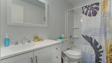 A bathroom with a white sink, two faucets, a mirror, a toilet, and a shower with a floral curtain.