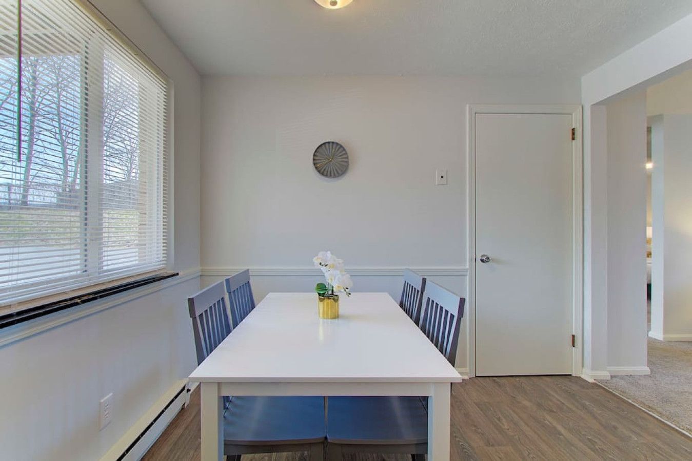 A dining area with a white table, blue chairs, a small plant, and a door to the right.