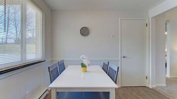 A dining area with a white table, blue chairs, a small plant, and a door to the right.