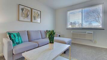 Un salon avec un canapé gris, une table basse blanche, une plante en pot et deux œuvres d’art encadrées accrochées au mur.