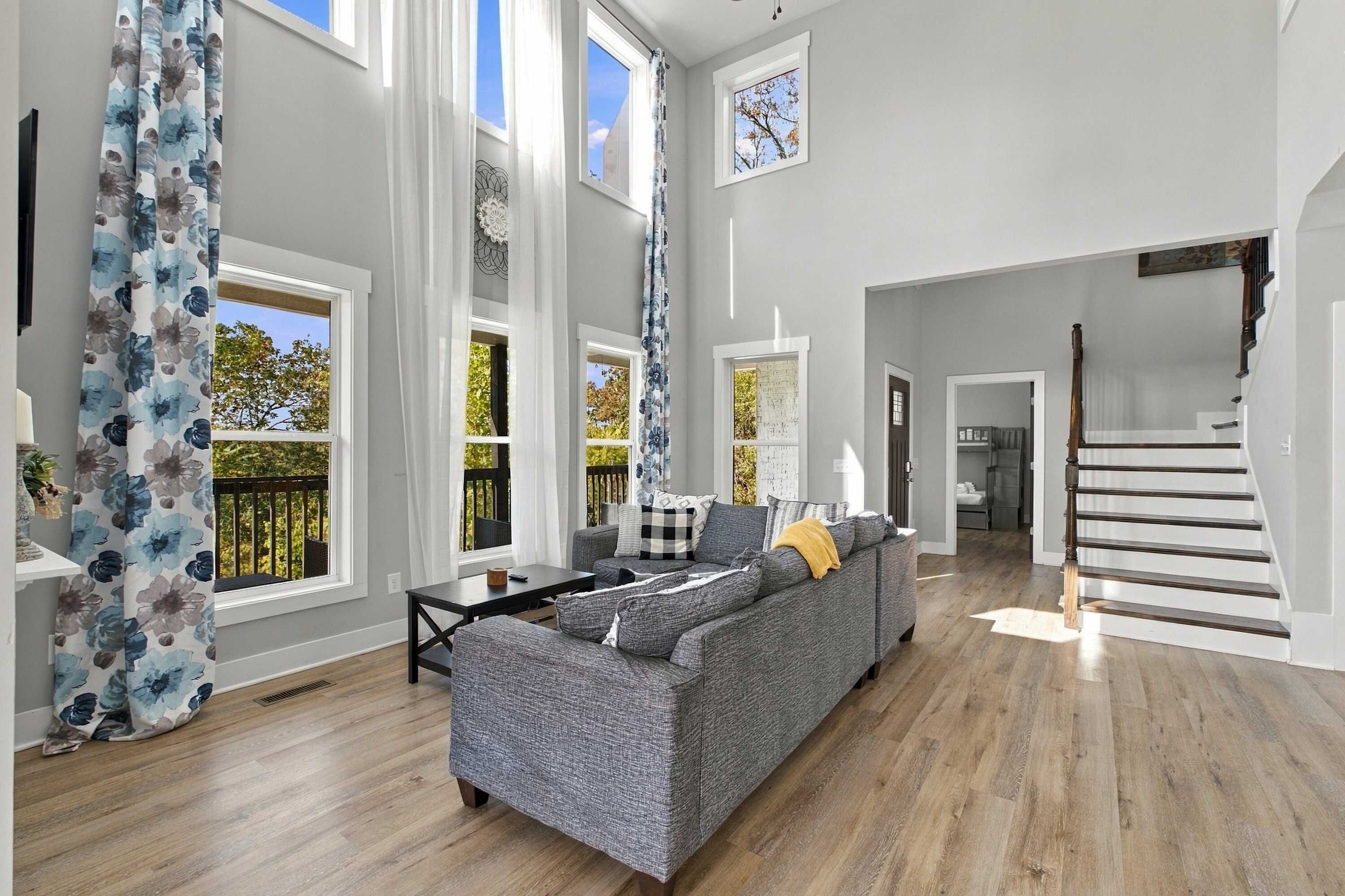 A spacious living room with a grey sofa, a coffee table, and a staircase leading to an upper level.