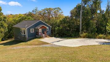 A small house with a porch, surrounded by trees and a concrete driveway.
