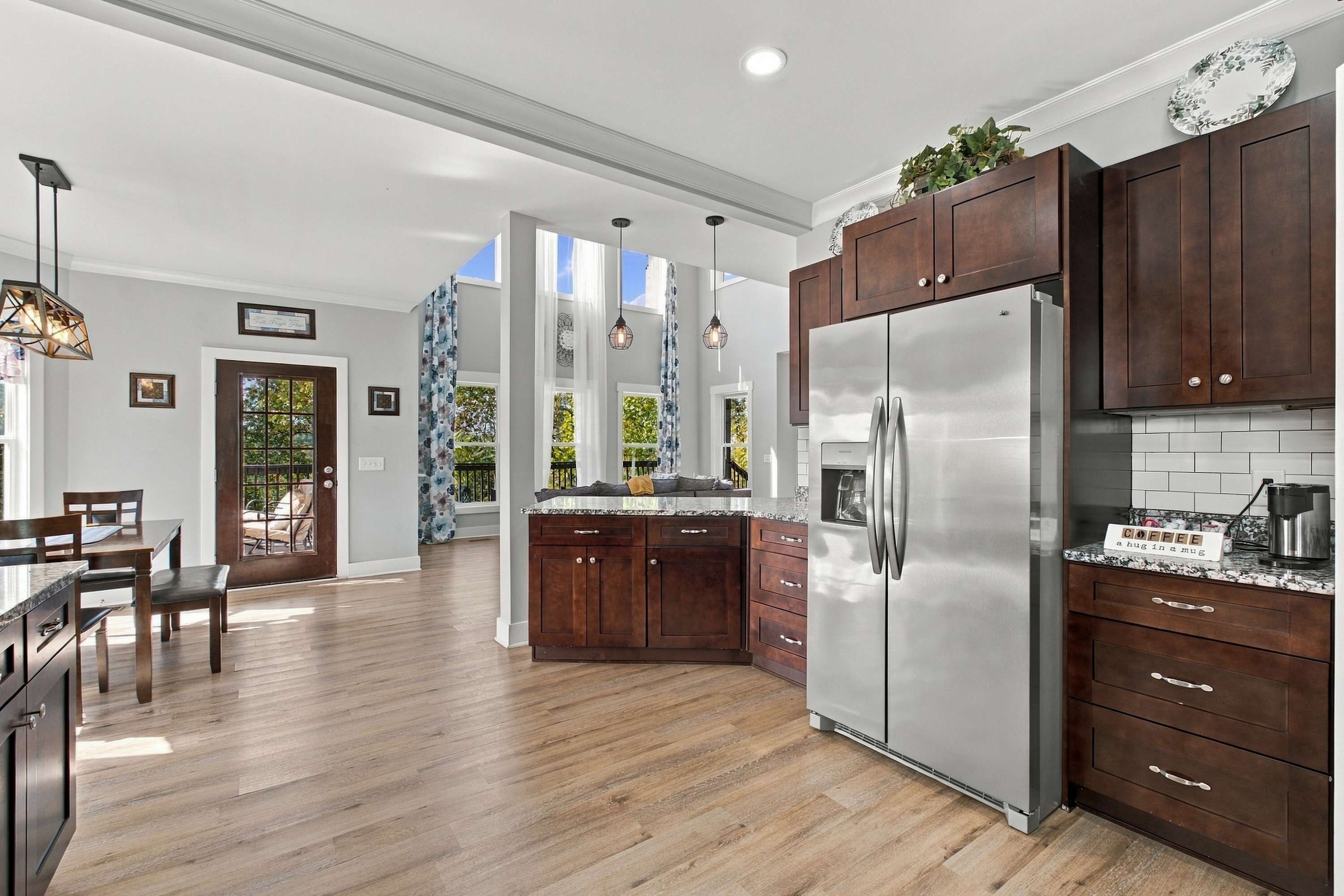A modern kitchen with wooden cabinets, a stainless steel refrigerator, and a dining area with a table and chairs.