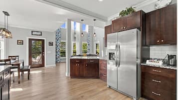 A modern kitchen with wooden cabinets, a stainless steel refrigerator, and a dining area with a table and chairs.