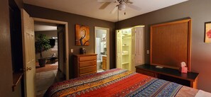 A bedroom with a bed, a dresser, a nightstand, a ceiling fan, and a walk-in closet.