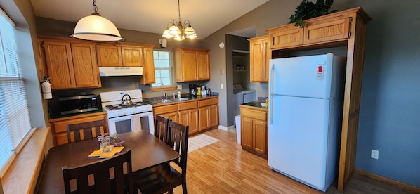 A kitchen with wooden cabinets, a stove, a microwave, a refrigerator, and a dining table with chairs. - Quiet 2BR Treehouse Loft Near Downtown Tahlequah (Tahlequah)
