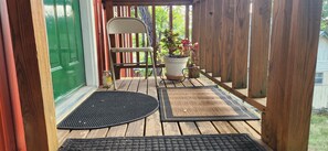 A wooden deck with a chair, a potted plant, and a doormat.