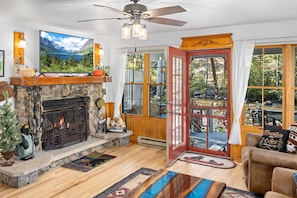 A cozy living room with a fireplace, a television, and a view of a mountain landscape. - River Front Escape, 3 Bedrooms on River, Quite area (Estes Park)