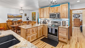 A kitchen with wooden cabinets, a granite countertop, stainless steel appliances, and a dining area with a wooden table and chairs. - River Front Escape, 3 Bedrooms on River, Quite area (Estes Park)