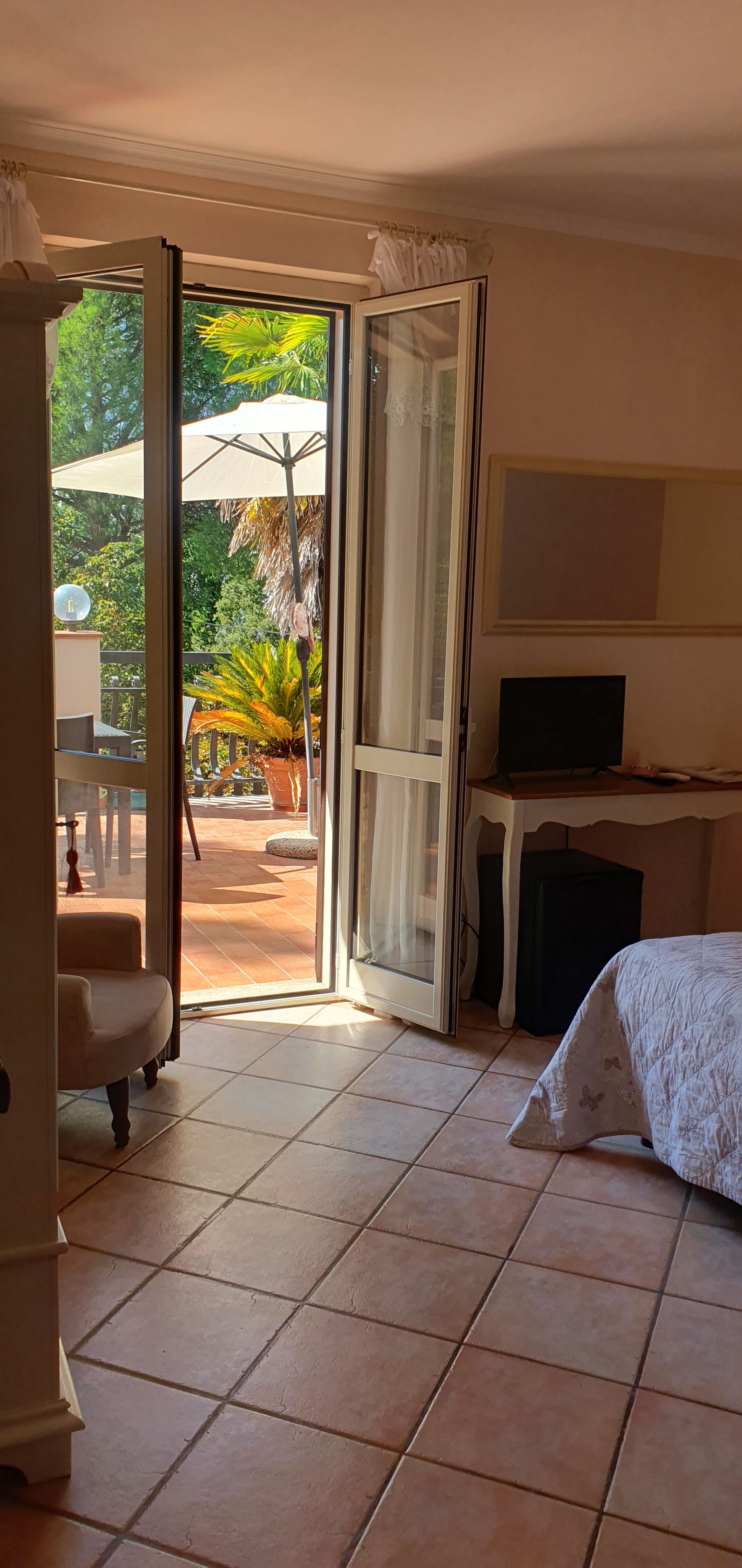 Ein Hotelzimmer mit Bett, Fernseher, Schreibtisch und Blick auf einen Garten mit einer Palme.