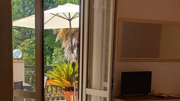 Ein Hotelzimmer mit Bett, Fernseher, Schreibtisch und Blick auf einen Garten mit einer Palme.