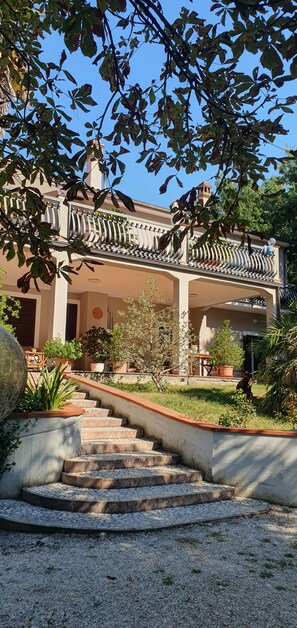 A building with a staircase leading to a covered entrance, surrounded by greenery and potted plants. - Located near the Marmore Falls, Villa Maria welcomes you to the Umbrian hills (Umbria)
