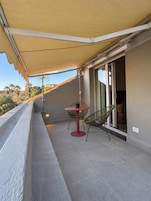 Varanda com mesa, cadeiras, porta de correr de vidro e toldo de proteção.