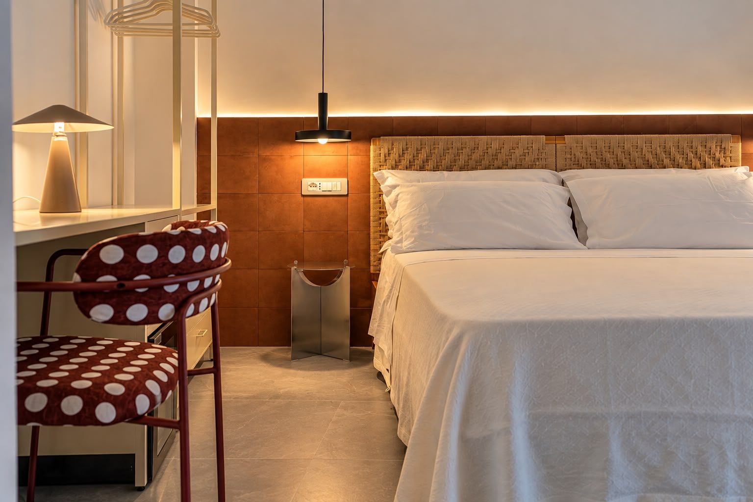 A hotel room with a bed, a desk, a chair, and a wall-mounted light fixture.