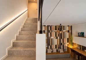 Eine Treppe mit modernem Design, eine Sitzecke mit geometrischem Wandmuster und ein Holztisch mit Stühlen.