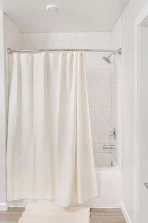 Un bagno con tenda da doccia, una vasca e un rivestimento in piastrelle bianche.