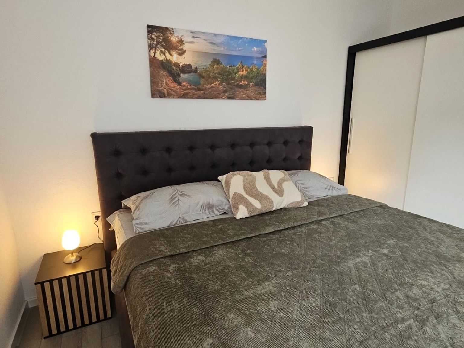 A bedroom with a bed, a nightstand, a lamp, and a painting on the wall.