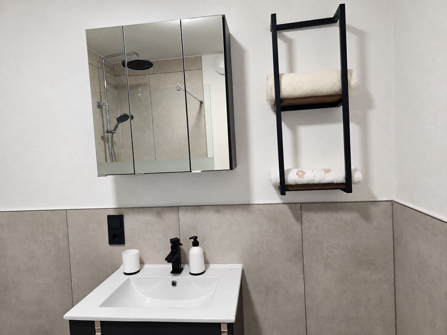 Ein Badezimmer mit einem weißen Waschbecken, einem Spiegel, einem Handtuchhalter und einer Dusche.