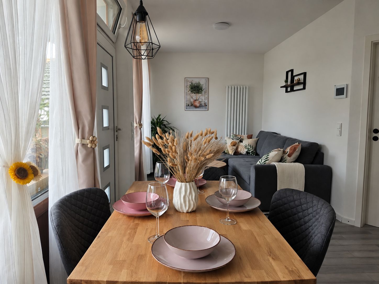 Un coin repas avec une table en bois, des assiettes roses et des verres à vin transparents.