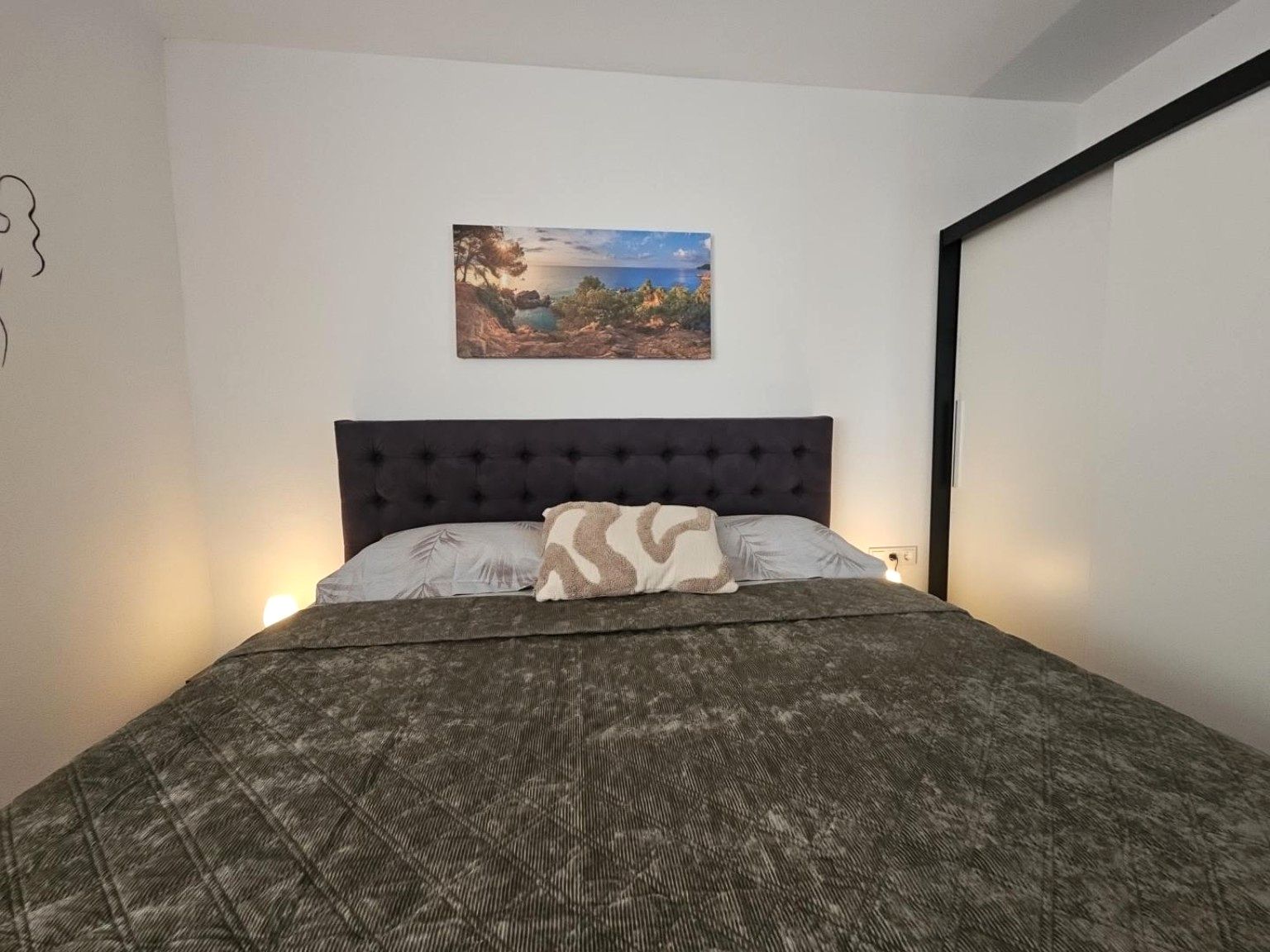 Une chambre à coucher avec un lit, une tête de lit, un tableau accroché au mur et une table de chevet avec une lampe.