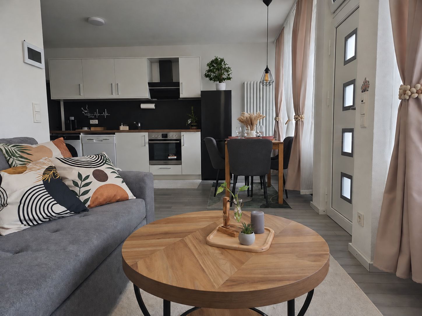 Un salon moderne avec un canapé gris, une table basse ronde en bois et un coin repas comprenant une chaise noire et une table en bois.