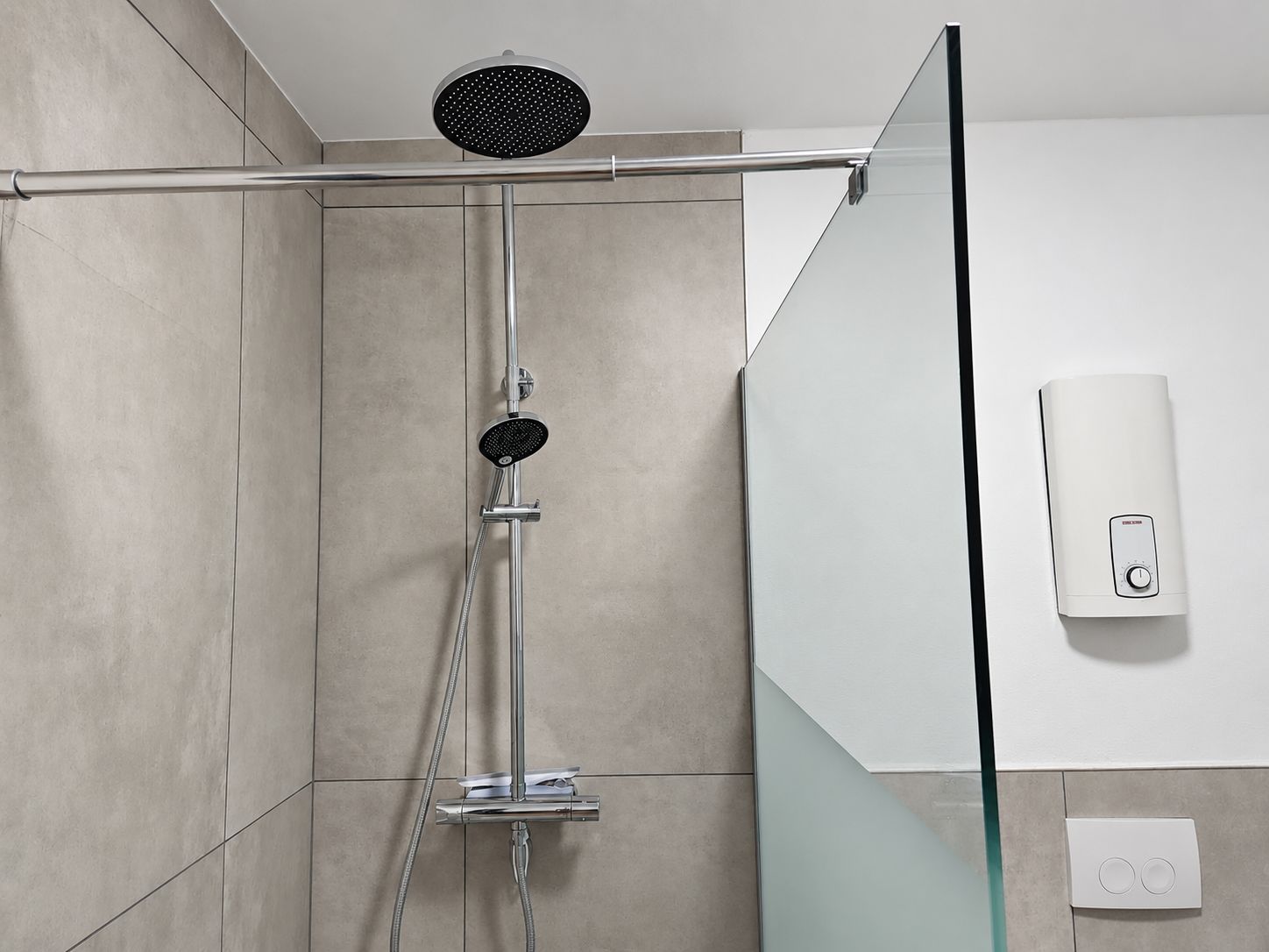 A shower enclosure with a handheld showerhead and a wall-mounted hand dryer.