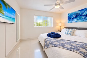 A hotel room with a bed, a ceiling fan, a window with blinds, a painting, and a TV on the wall. - Private Pool BBQ Outdoor Dining (Hollywood)