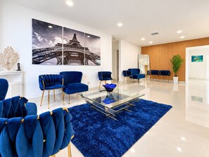 A modern hotel lobby with a glass coffee table, blue upholstered chairs, a large framed picture of the Eiffel Tower, and a wooden accent wall. - Private Pool BBQ Outdoor Dining (Hollywood)