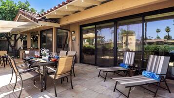 An outdoor patio with a table set for dining, chairs, and a covered seating area.